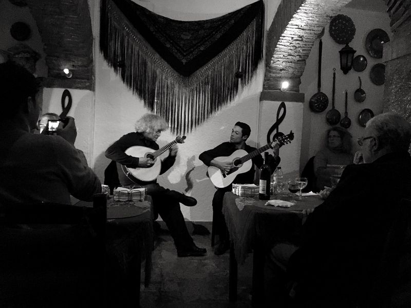 Two guitarists performing traditional fado in a dimly lit tavern in Alfama, Lisbon