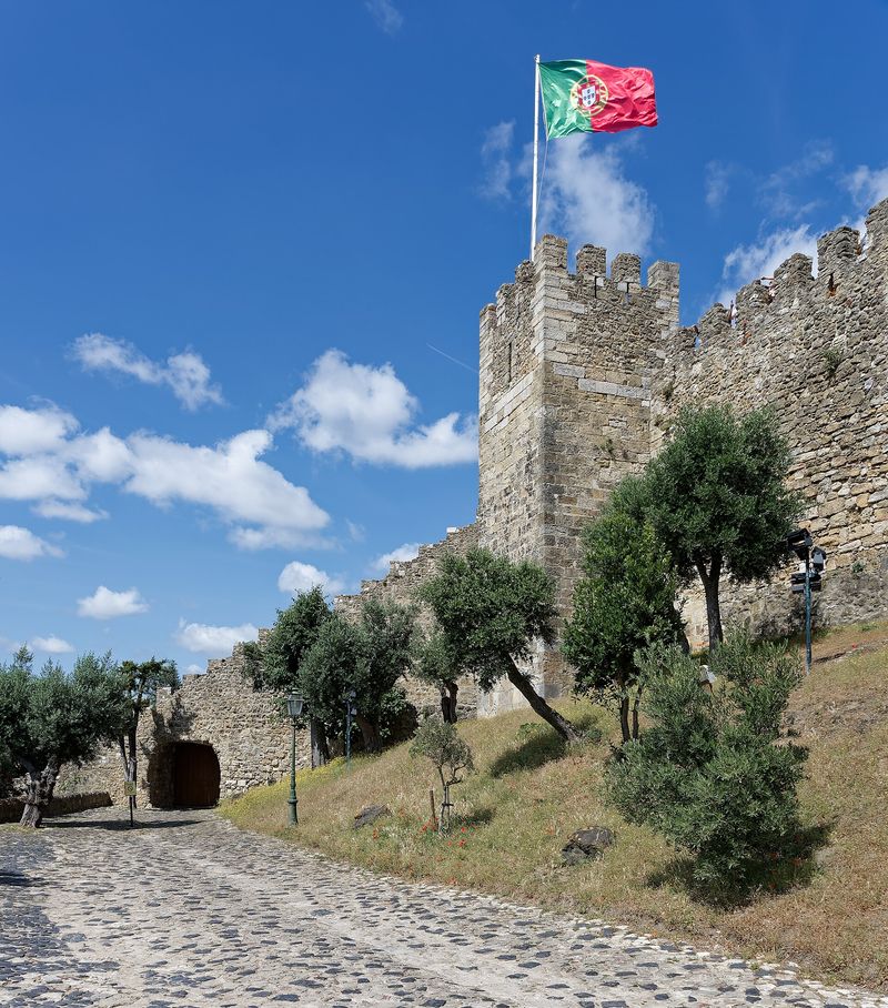 The stone ramparts and battlemented tower of the Castelo de São Jorge flying the Portuguese flag above Lisbon