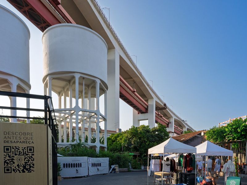 The white water towers and weekend market stalls of LX Factory beneath the great red Ponte 25 de Abril bridge, Lisbon