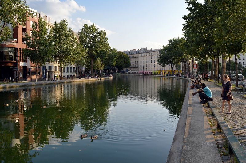 Tree-lined water of the Canal Saint-Martin with people relaxing on the quay in Paris