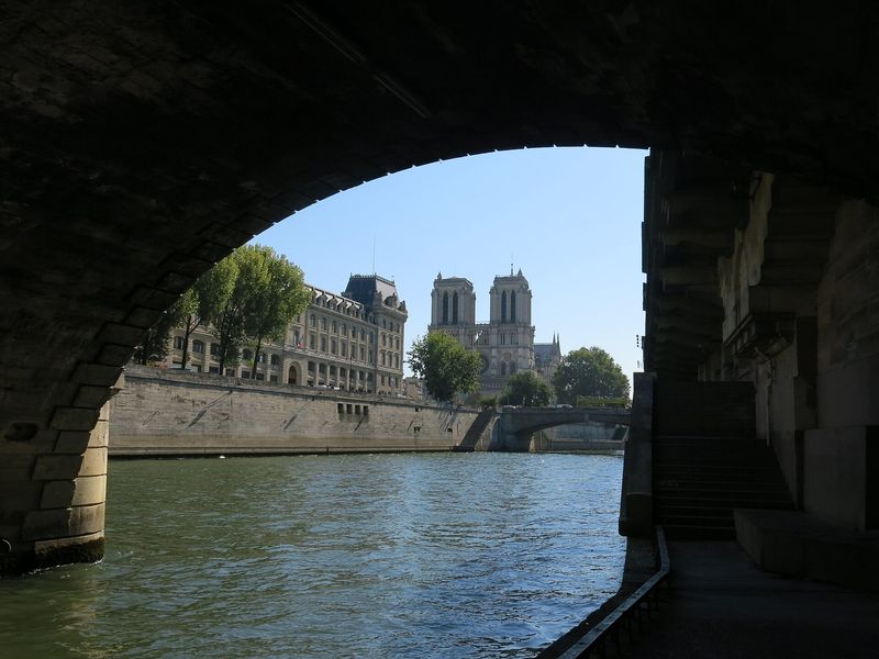 The towers of Notre-Dame rising above the Seine, framed by a bridge arch and the riverside quai in Paris