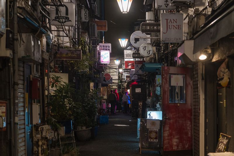 A narrow lantern-lit alley of tiny bars in Golden Gai, Shinjuku, Tokyo, at night, crowded with hand-painted signs
