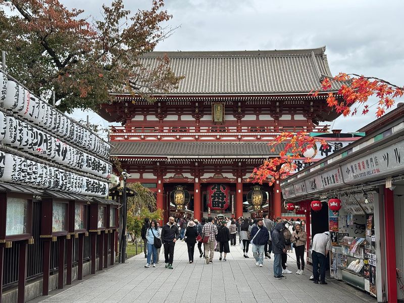 The vermilion Hōzōmon gate of Sensō-ji temple in Asakusa, Tokyo, framed by lantern-hung Nakamise stalls and autumn maple leaves