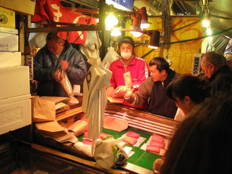 A busy fish and seafood stall in the Tsukiji Outer Market, Tokyo, with vendors and fresh tuna on display