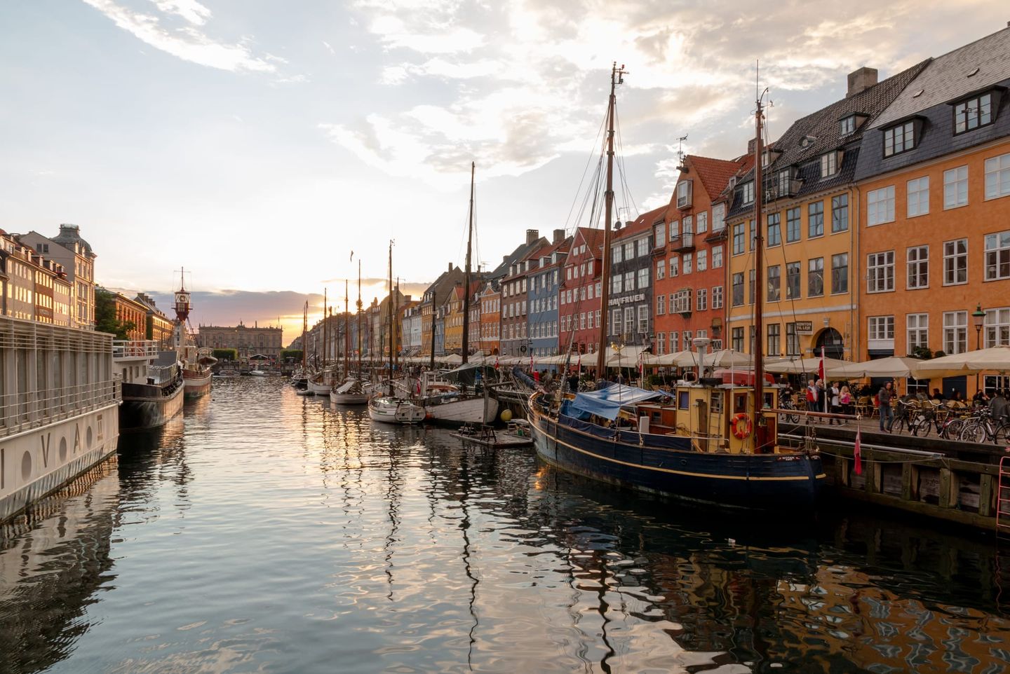 The colourful gabled townhouses of Nyhavn reflected in the canal at golden hour, with moored wooden boats lining the quay in Copenhagen