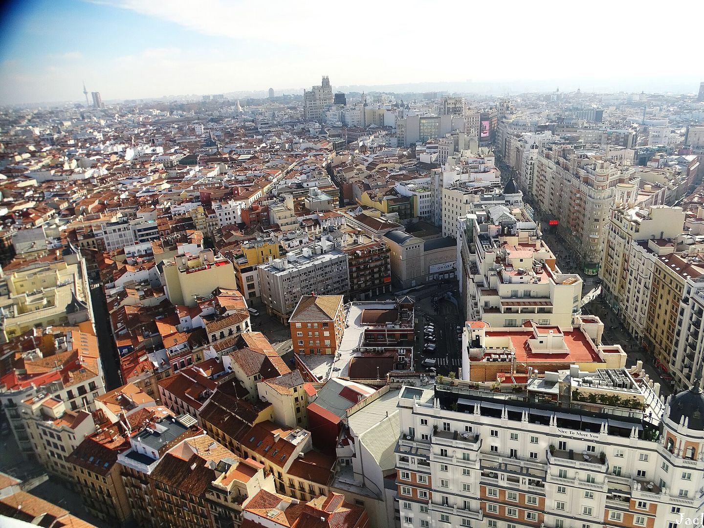 Aerial view over the terracotta rooftops of Madrid's historic centre toward the Telefónica building on Gran Vía, seen from a rooftop viewpoint near Callao