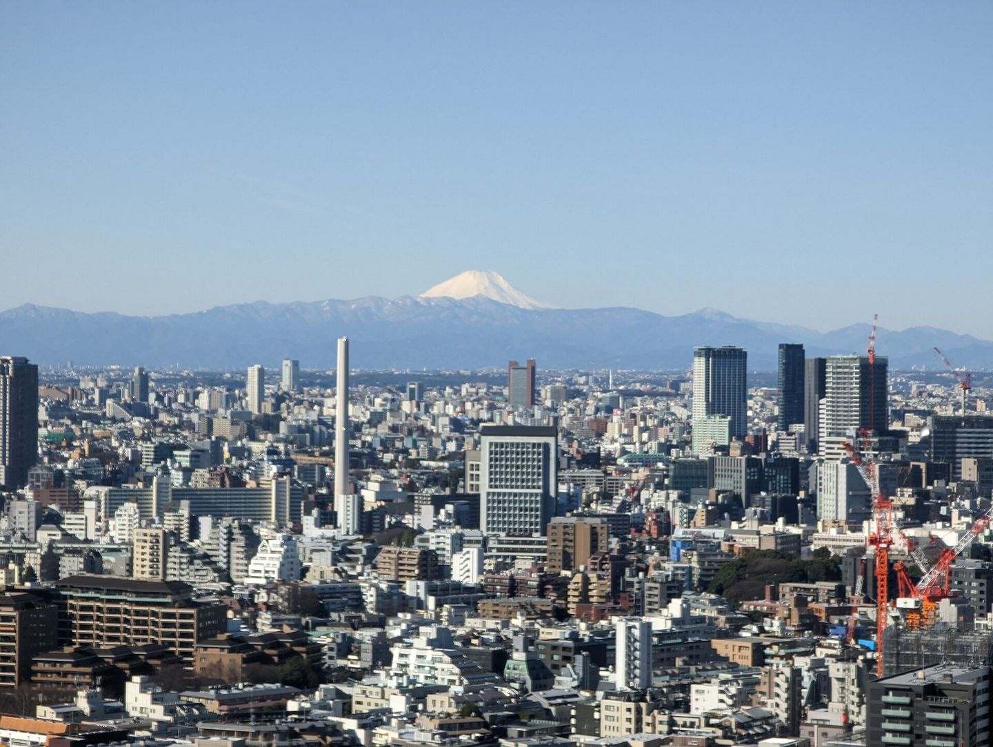 The dense Tokyo cityscape stretching to the horizon, with the snow-capped cone of Mount Fuji rising beyond the skyline under a clear blue sky