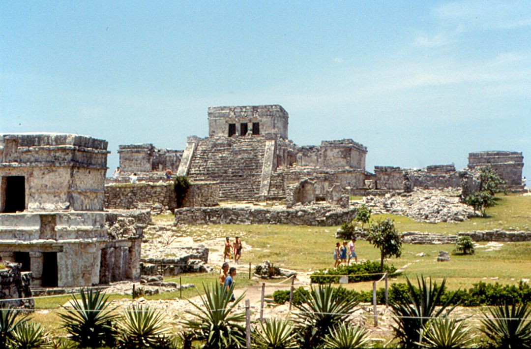 The Castillo pyramid of the Tulum Mayan ruins standing on a limestone cliff above the turquoise Caribbean Sea, with the Temple of the Frescoes visible at left