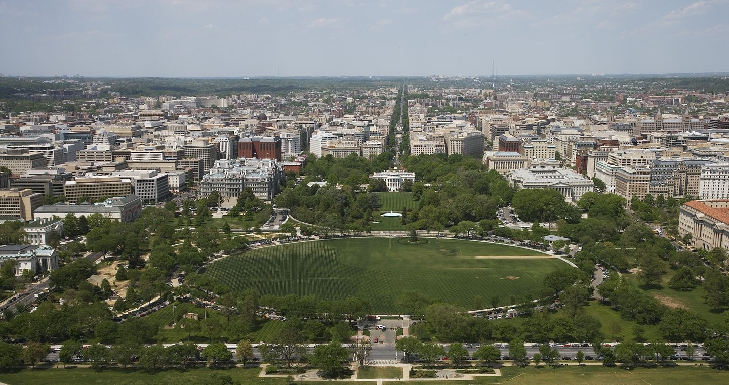 Aerial view over downtown Washington, D.C. looking toward the White House, with the National Mall and its museums and monuments stretching into the distance